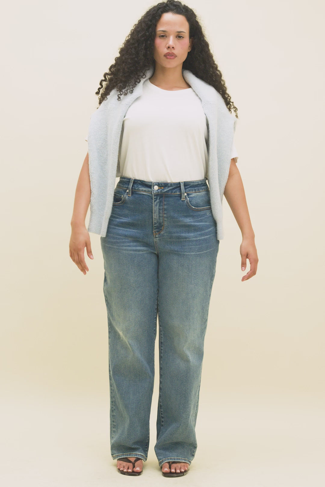 Video of a woman wearing a white t-shirt and blue jeans with a light blue sweater draped over her shoulders.