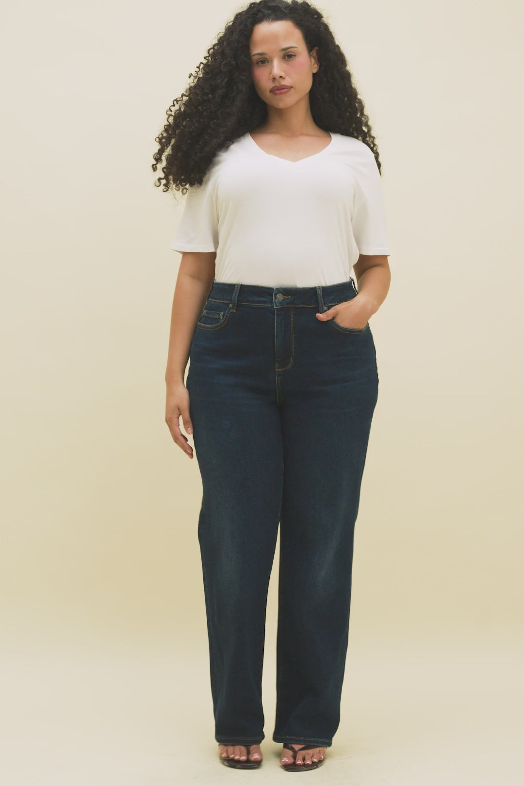 Video of a woman wearing a white v-neck t-shirt and straight leg dark jeans.