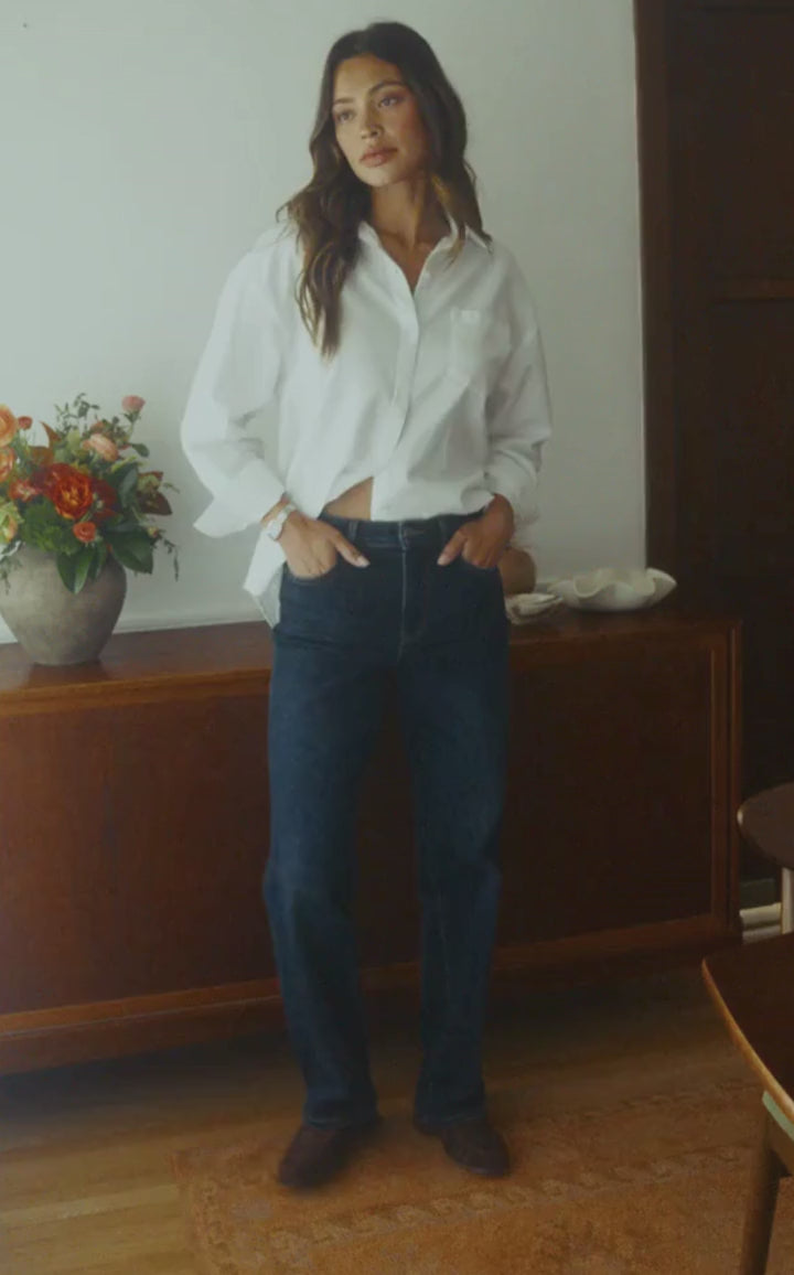 Woman in motion inside a dining room wearing dark jeans and a white button up top