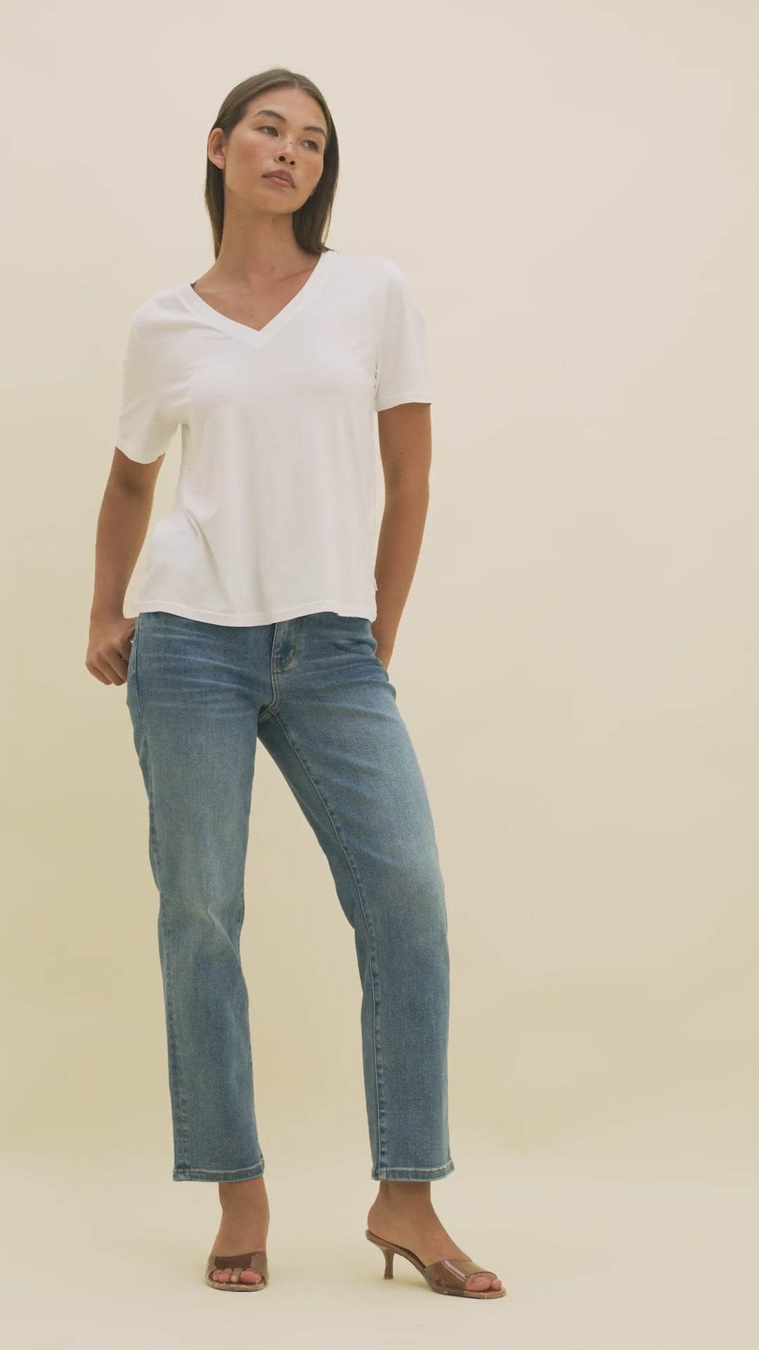 Video of a woman wearing medium wash straight cropped jeans and a white v-neck t-shirt