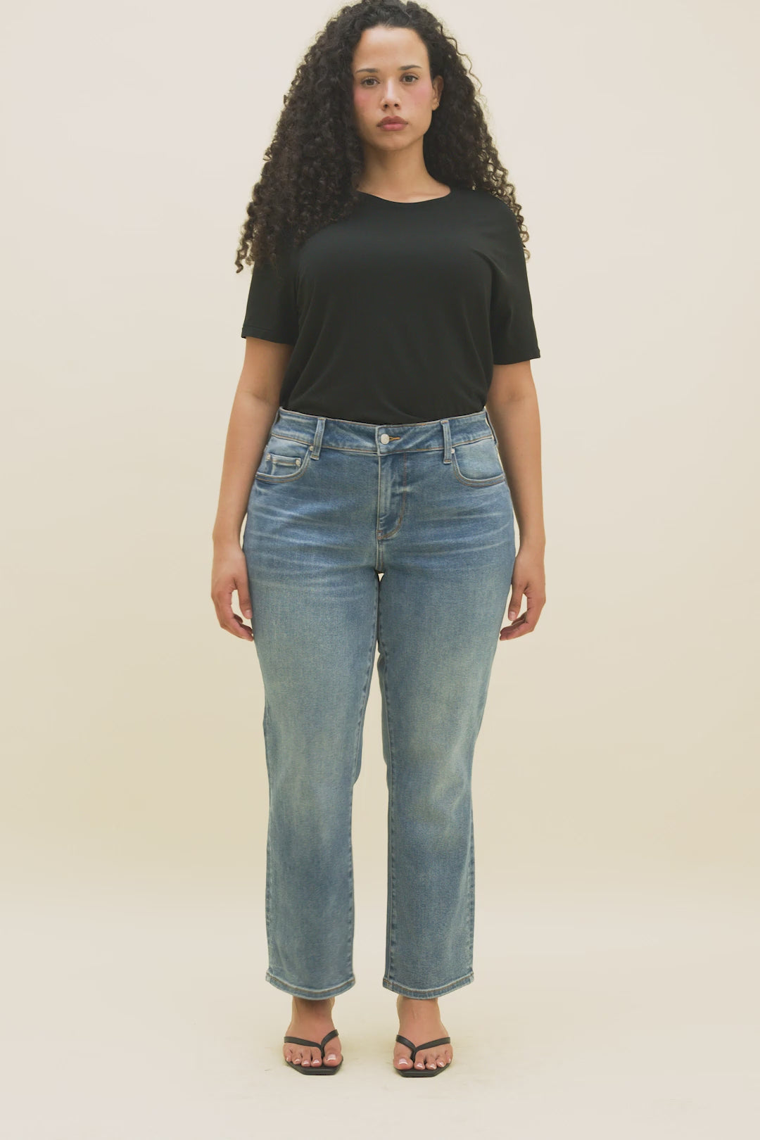 Video of a woman wearing a black t-shirt and medium blue cropped straight leg jeans.