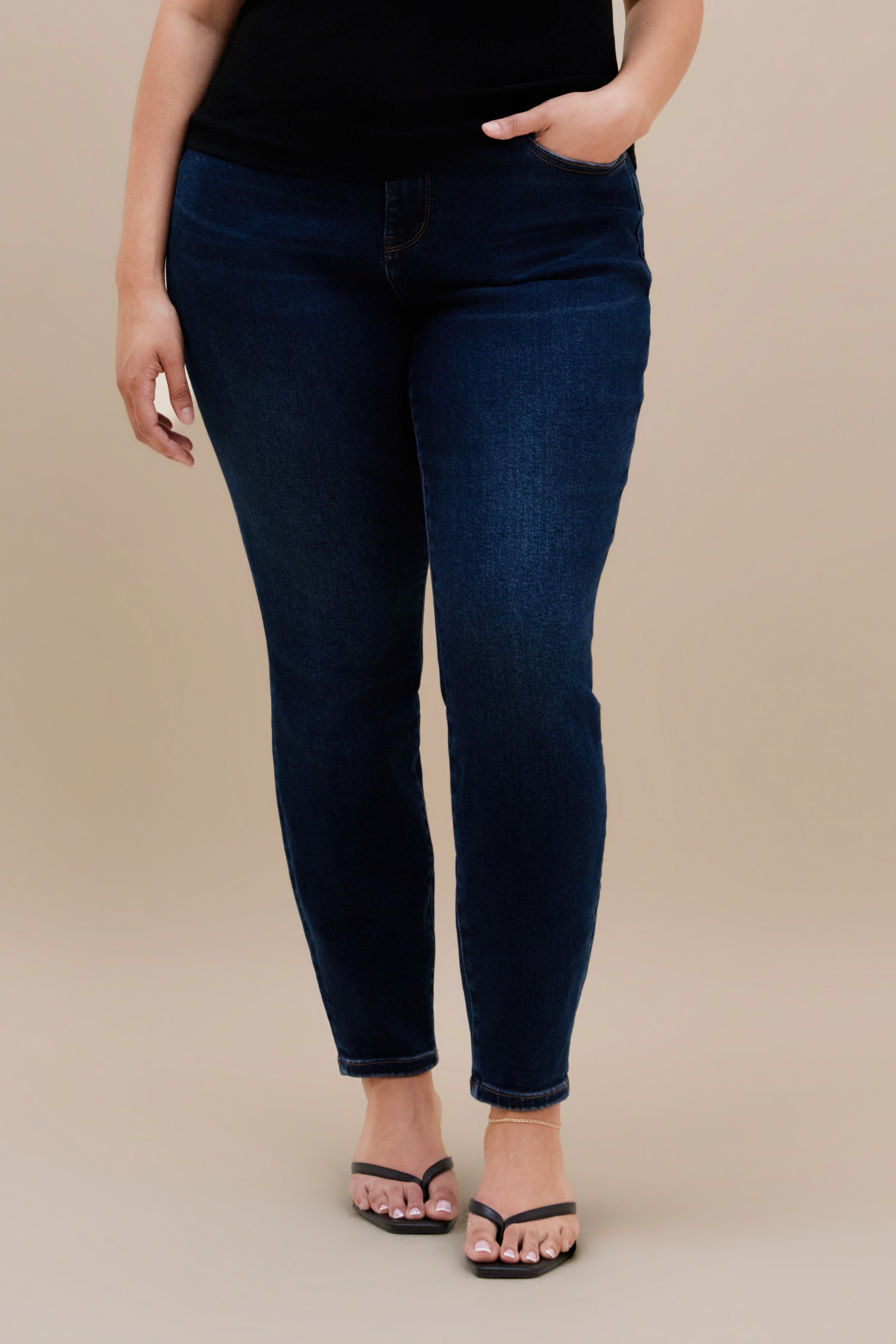 Bottom close up of dark skinny jeans against a beige background
