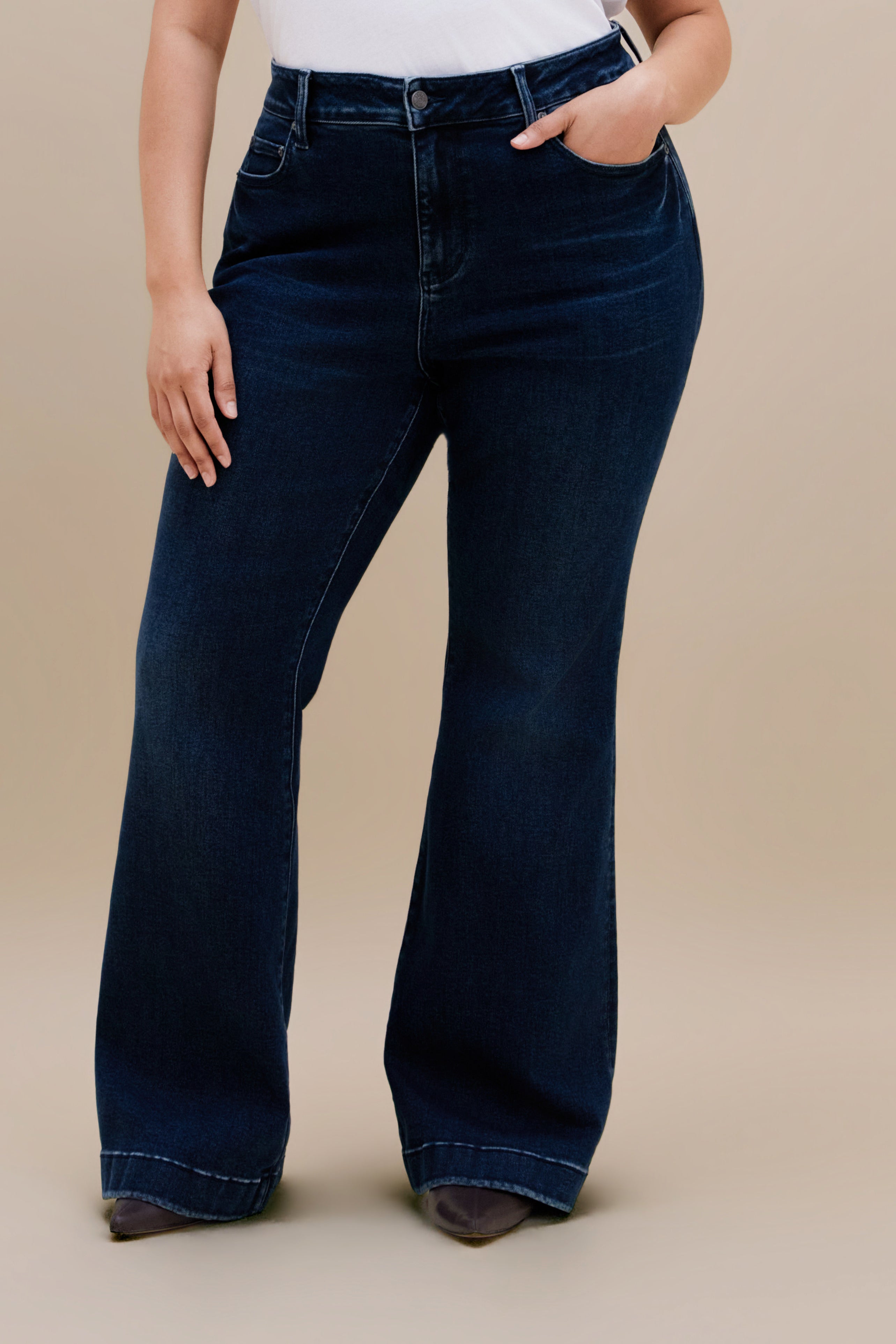 Bottom close up of dark flare jeans against a beige background